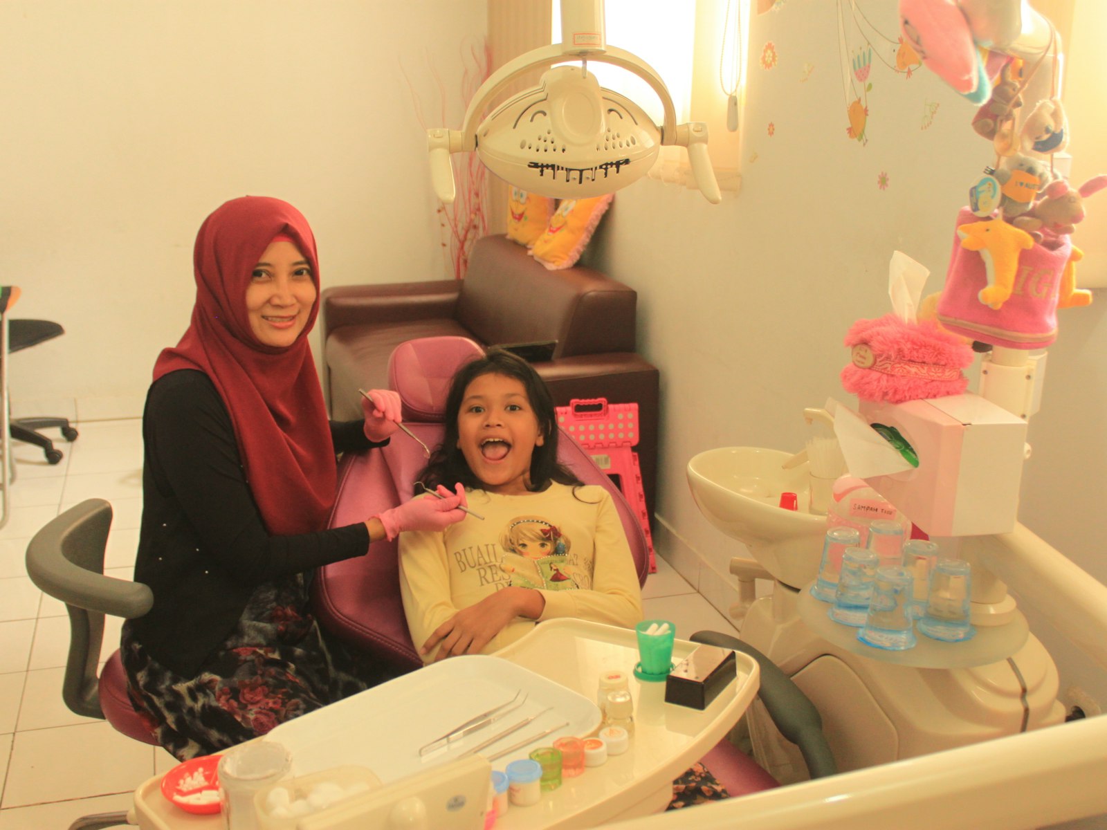 Niña sonriendo en el sillón del dentista junto a su madre
